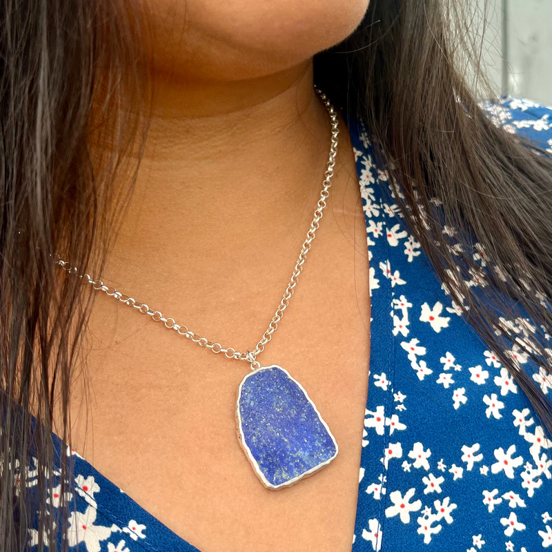 Woman in a blue floral top wearing a raw lapis lazuli slice pendant on sterling silver rolo chain