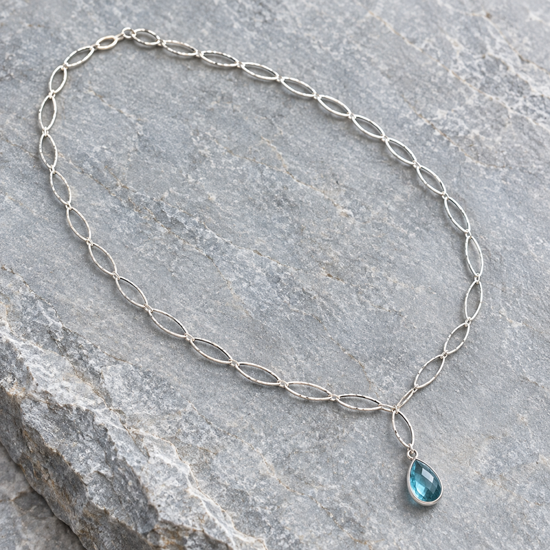 Aqua blue topaz teardrop necklace on sterling silver marquise chain, laid flat on stone