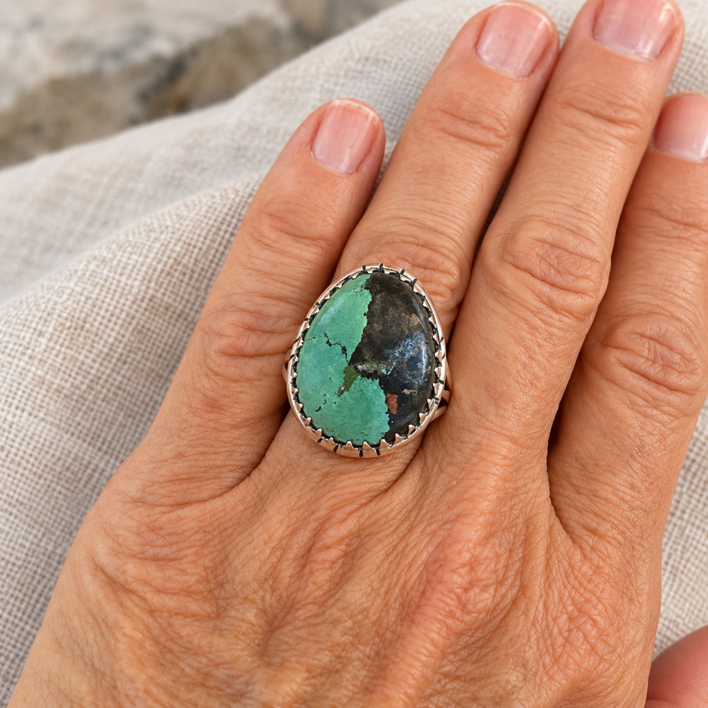 Green turquoise oval ring with black matrix in a sawtooth sterling silver bezel, front product view.