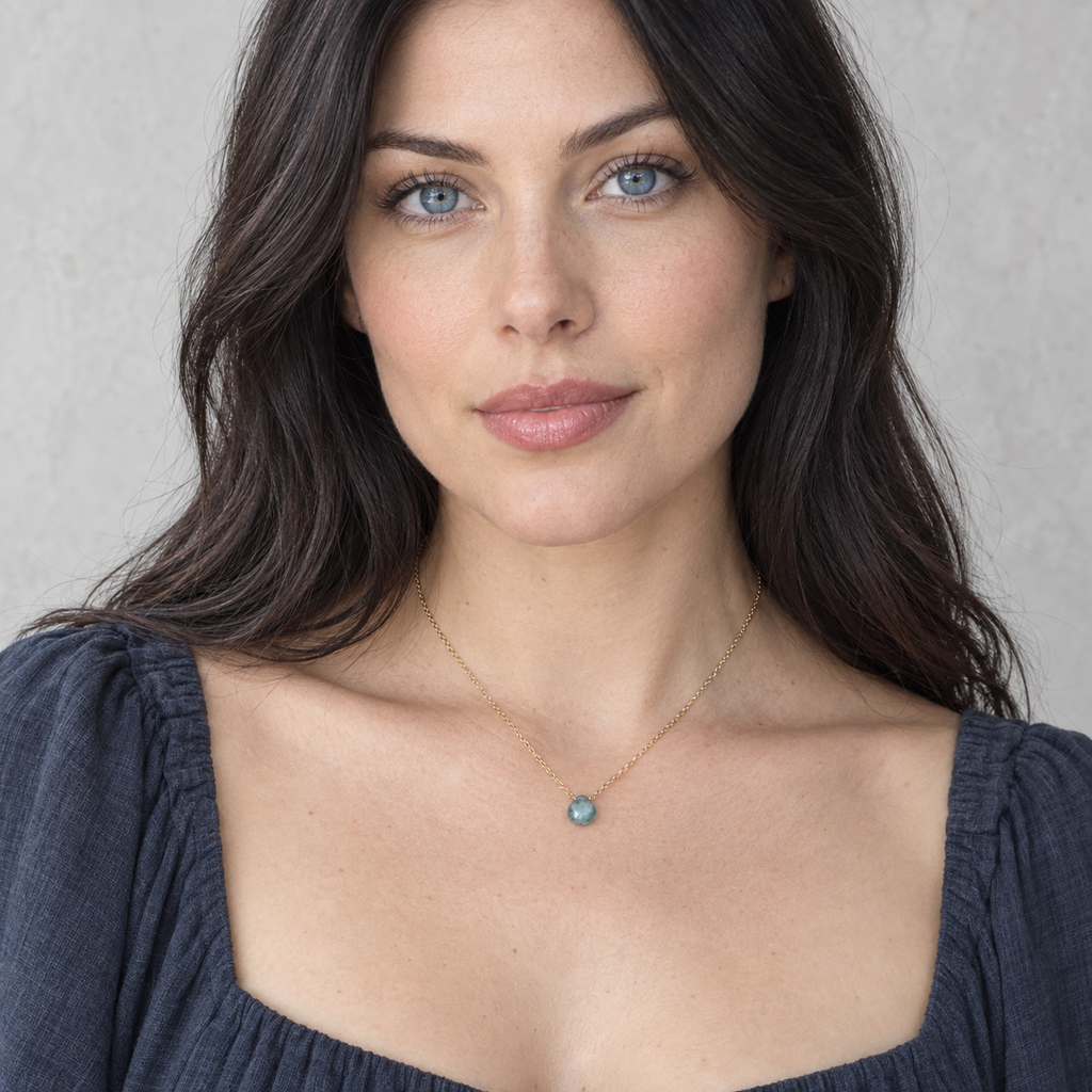 Full view of a delicate gold chain necklace with a faceted blue-green gemstone pendant