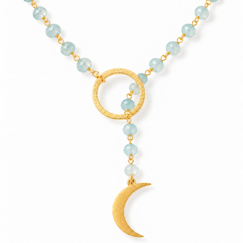 Close-up of faceted milky aquamarine beads passing through a hammered gold circle above a gold crescent moon
