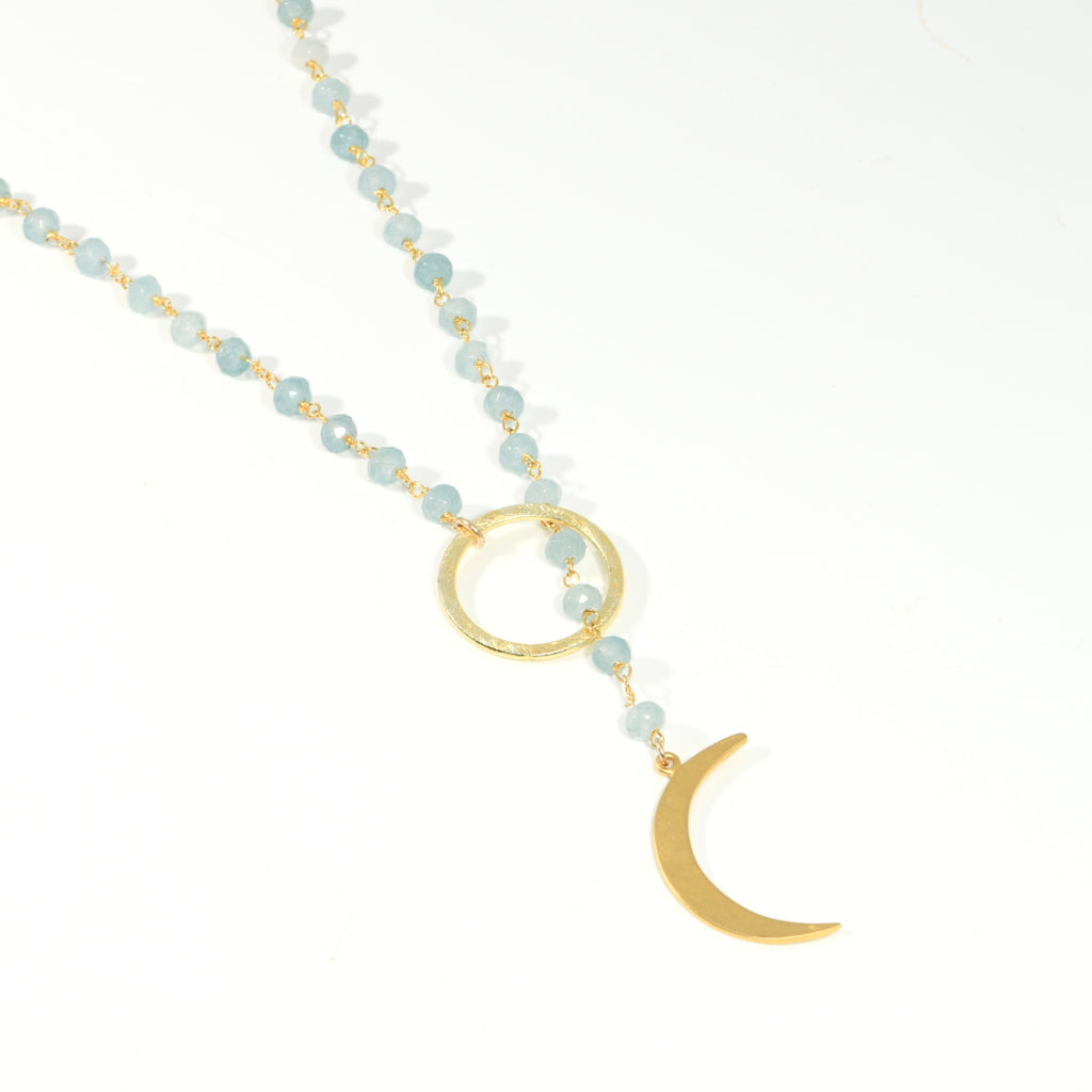 Close-up of faceted milky aquamarine beads passing through a hammered gold circle above a gold crescent moon